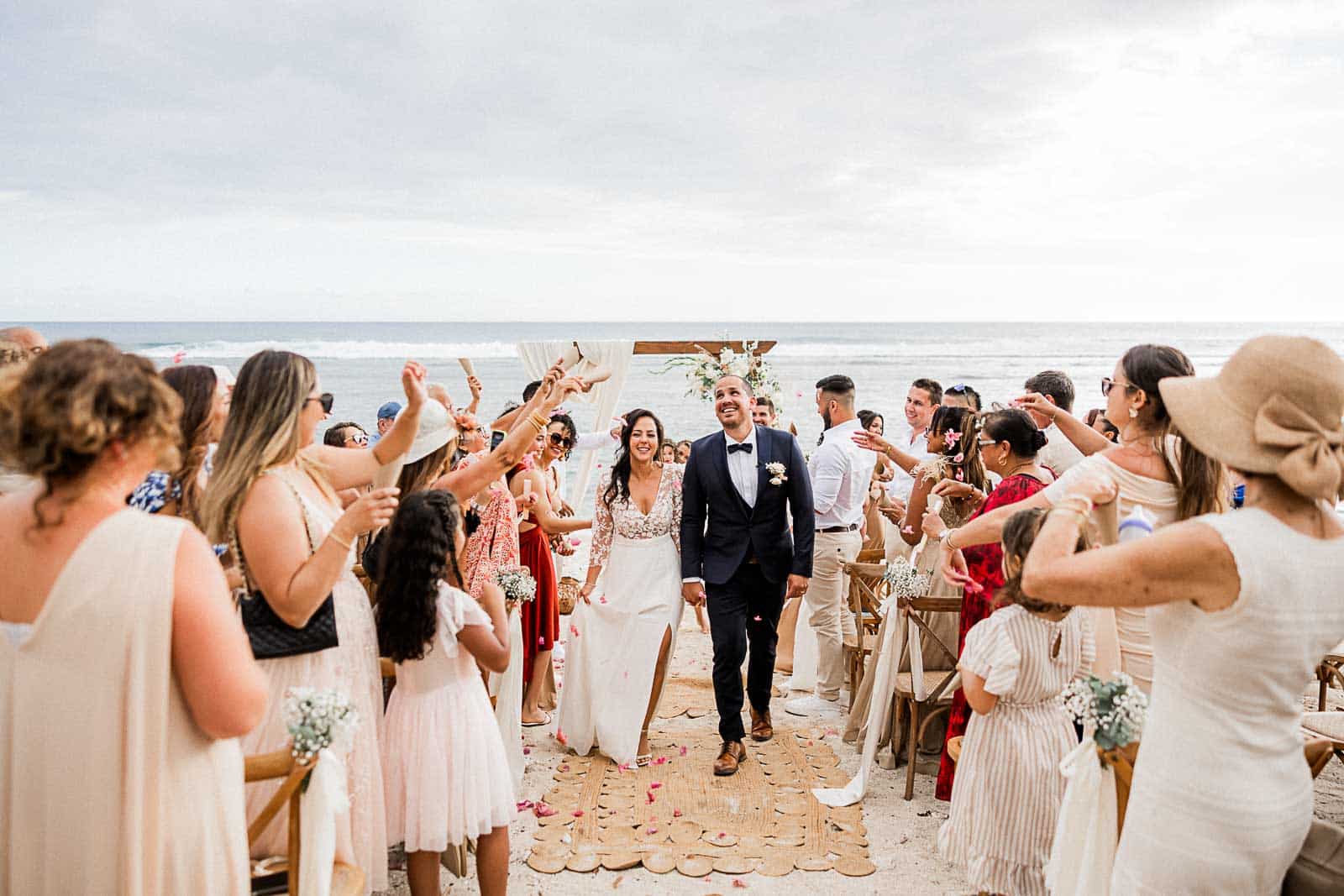 Photographie de Mathieu Dété, photographe de mariage sur l'île de la Réunion 974, présentant un couple de mariés sortant de la cérémonie laïque sur la plage de Saint-Leu