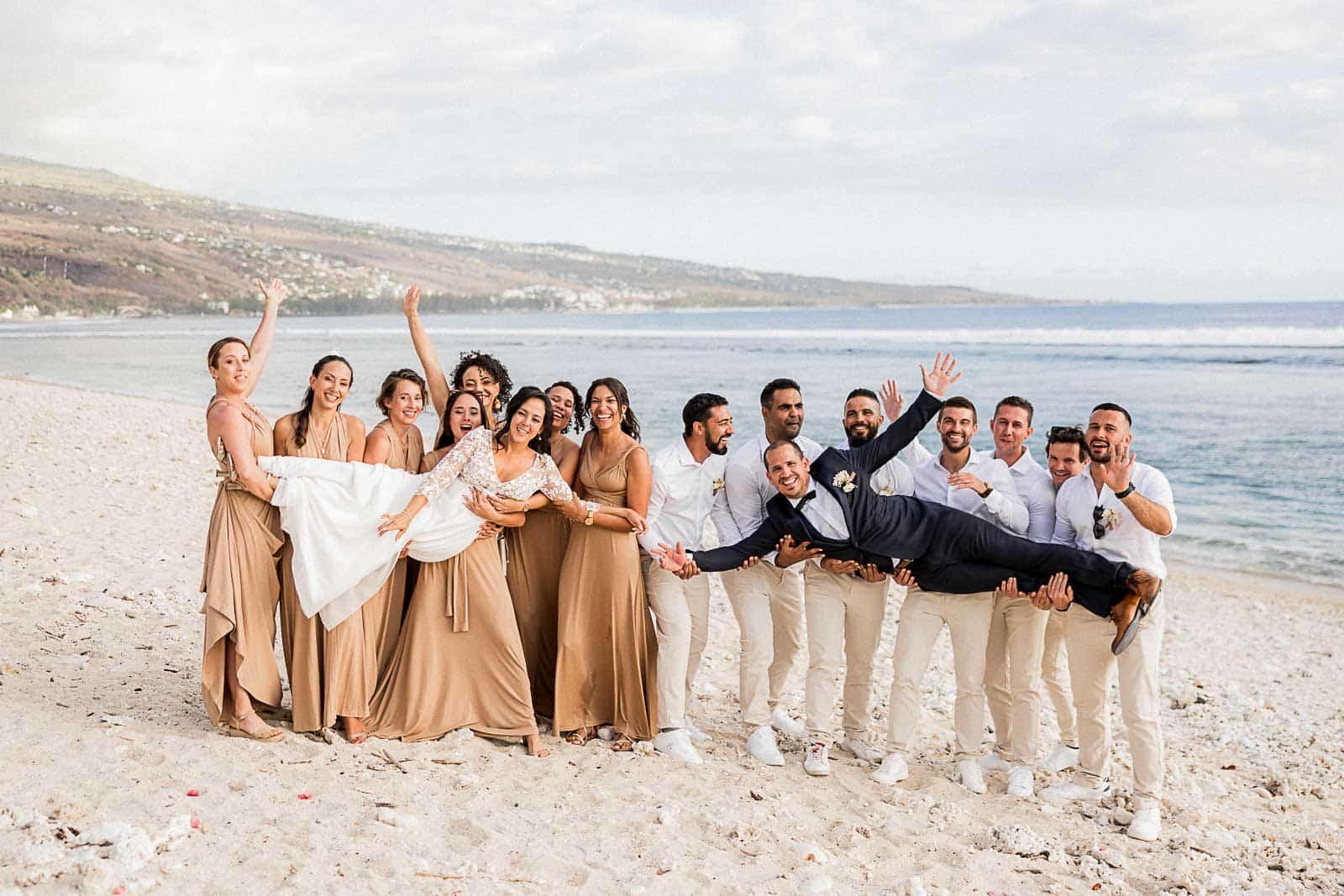 Photographie de Mathieu Dété, photographe de mariage sur l'île de la Réunion 974, présentant une photo de groupe avec les garçons et les demoiselles d'honneur portant les mariés sur la plage de Saint-Leu
