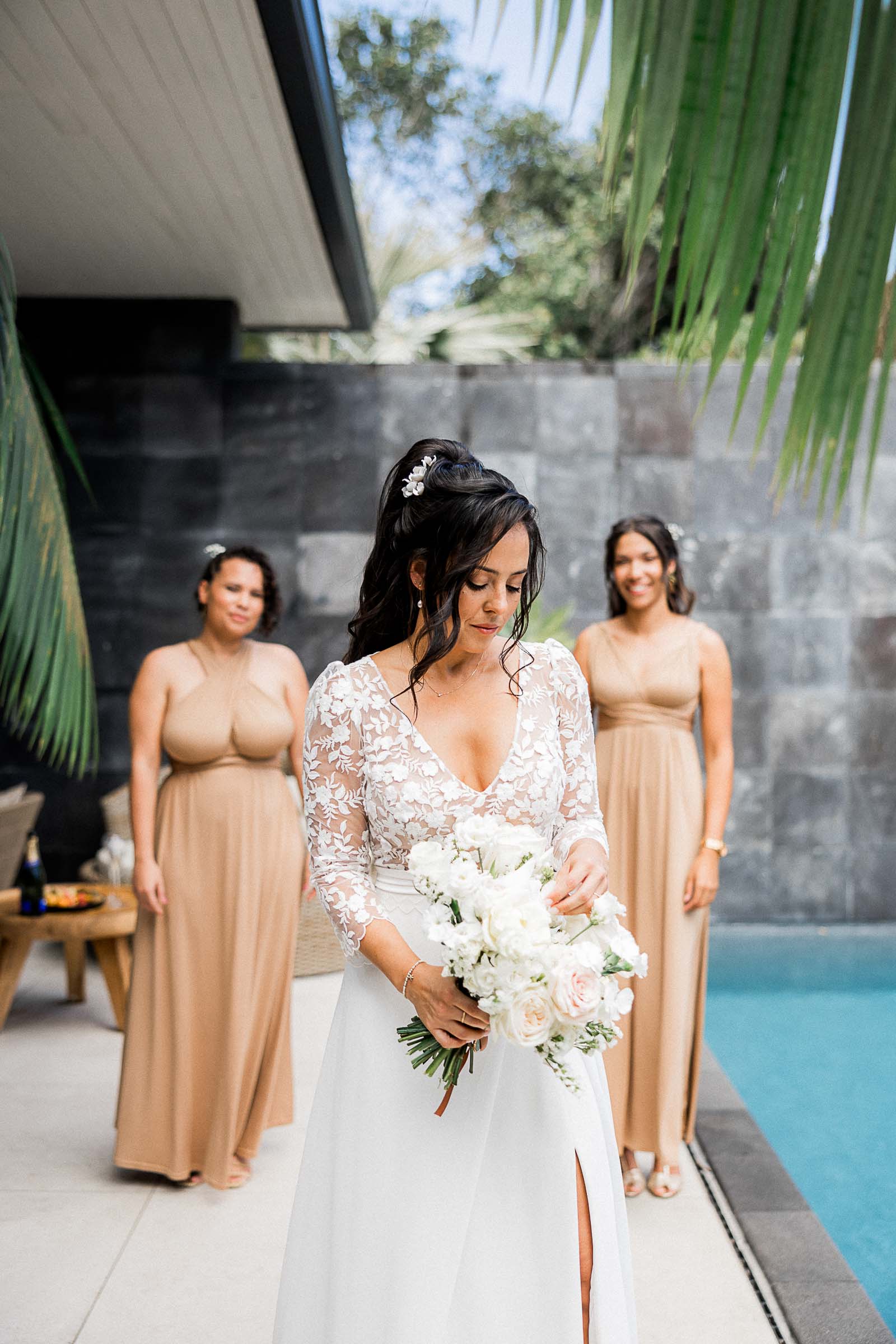 Photographie de Mathieu Dété, photographe de mariage sur l'île de la Réunion 974, présentant la mariée avec son bouquet, et ses témoins en arrière plan, durant les préparatifs du mariage, au Palm