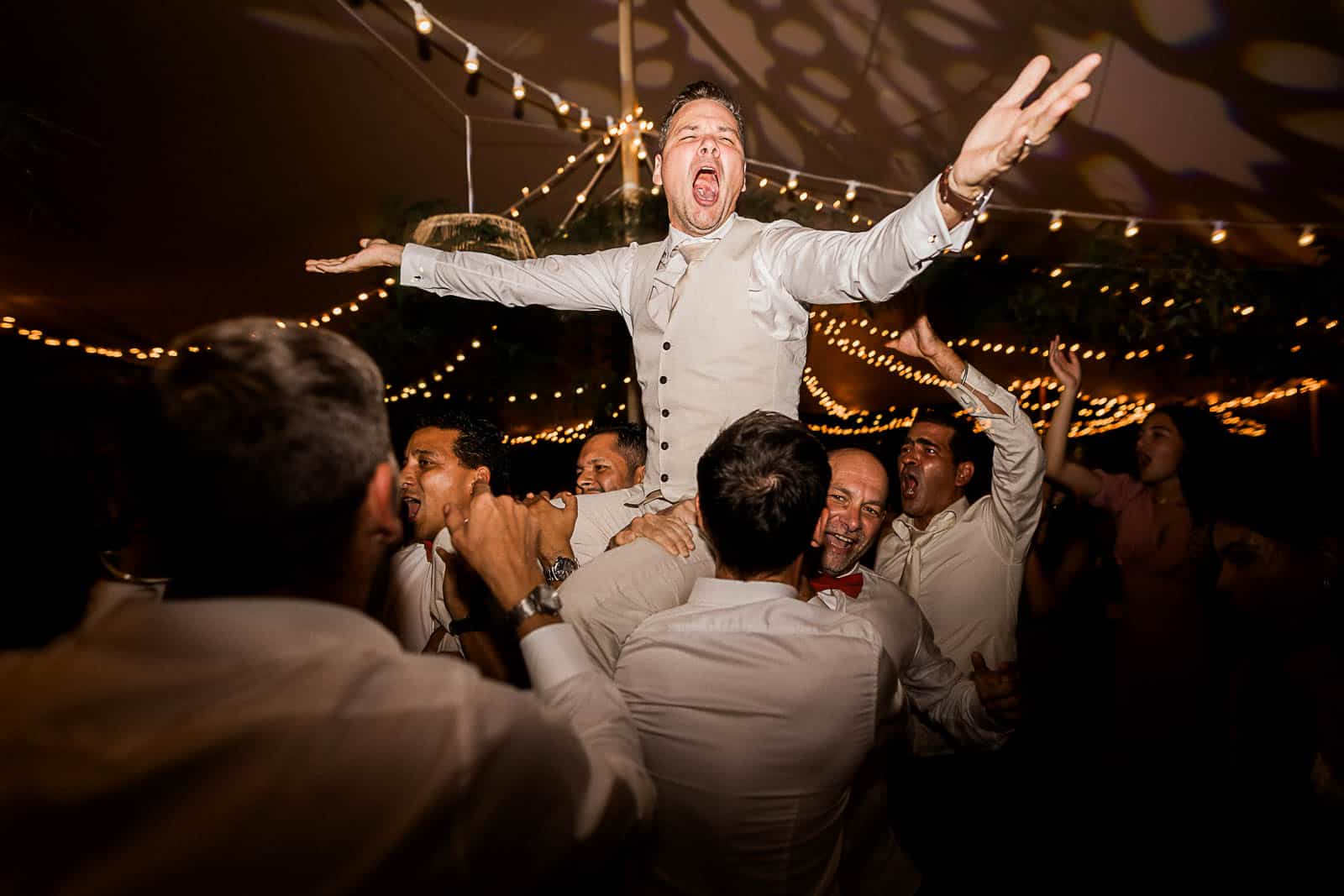 Photographie de Mathieu Dété, photographe de mariage et famille à Saint-Gilles sur l'île de la Réunion 974, présentant un marié porté par ses amis lors de la soirée du mariage au Jardin d'Eden