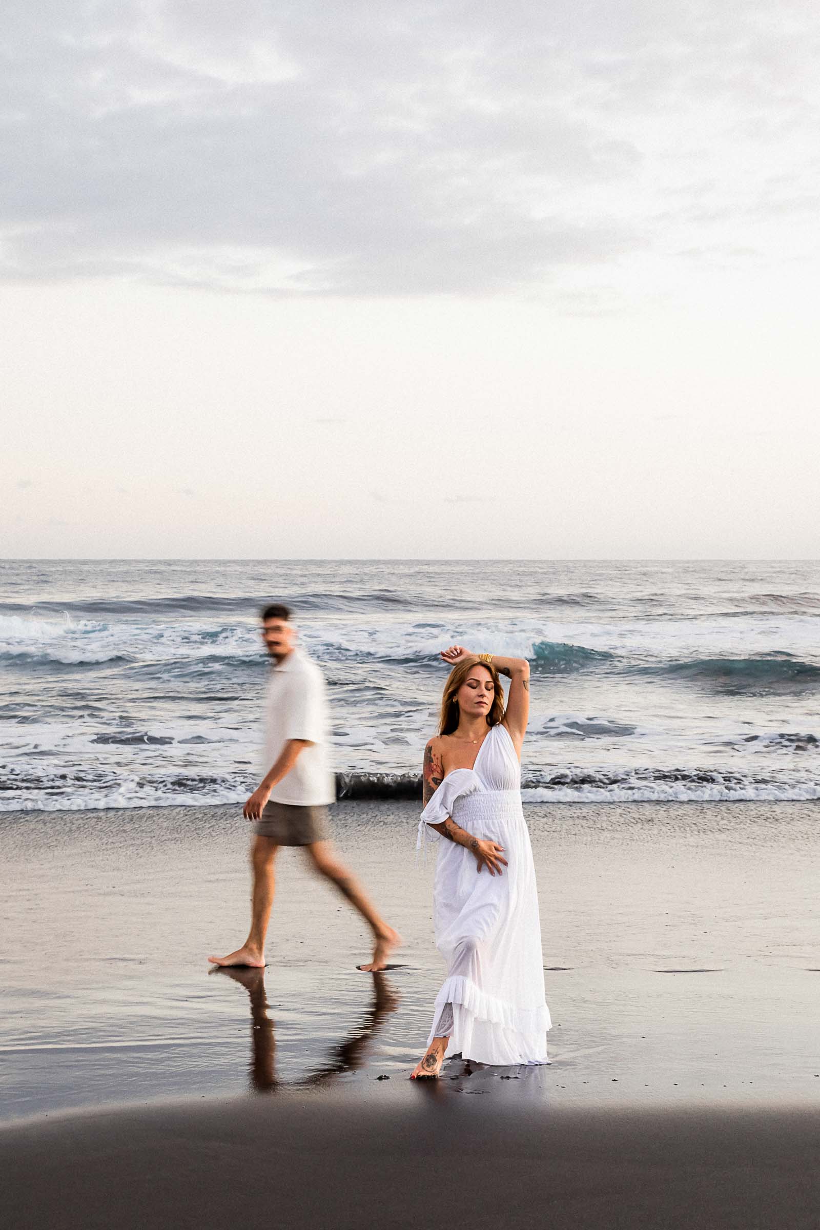 Photographie de Mathieu Dété, photographe de mariage sur l'île de la Réunion 974, présentant une femme posant face au photographe et son compagnon marchant derrière elle, sur la plage de la Ravine des Sables, à Etang Salé