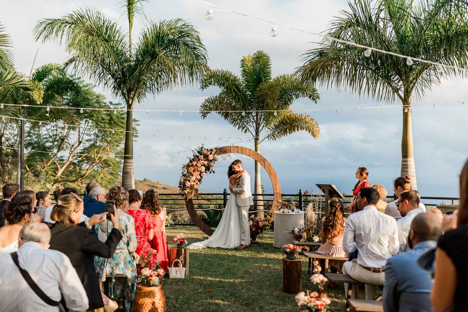 Photographie de Mathieu Dété, photographe de mariage et grossesse à Sainte-Marie, sur l'île de la Réunion 974, présentant les mariés enlacés sous l'arche de la cérémonie laïque, au Jardin d'Ama à Saint-Leu