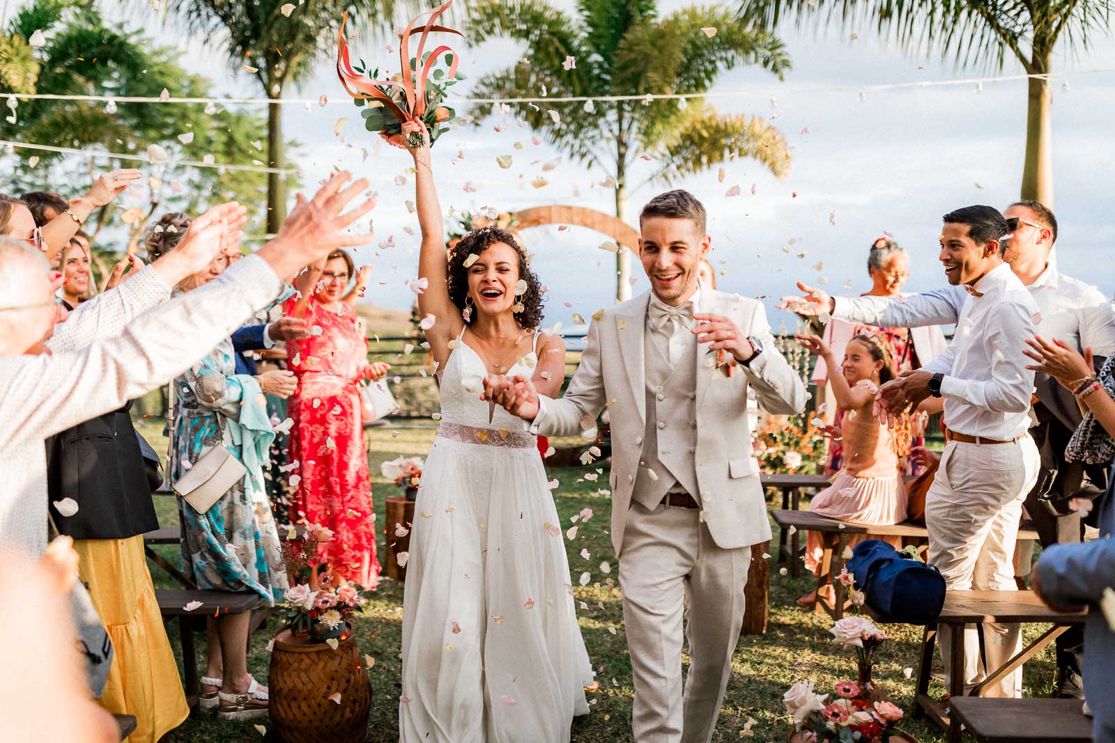 Photographie de Mathieu Dété, photographe de mariage et grossesse à Sainte-Marie, sur l'île de la Réunion 974, présentant la sortie de la cérémonie laïque des mariés, pleine de joie, sous les lancers de pétales de fleurs