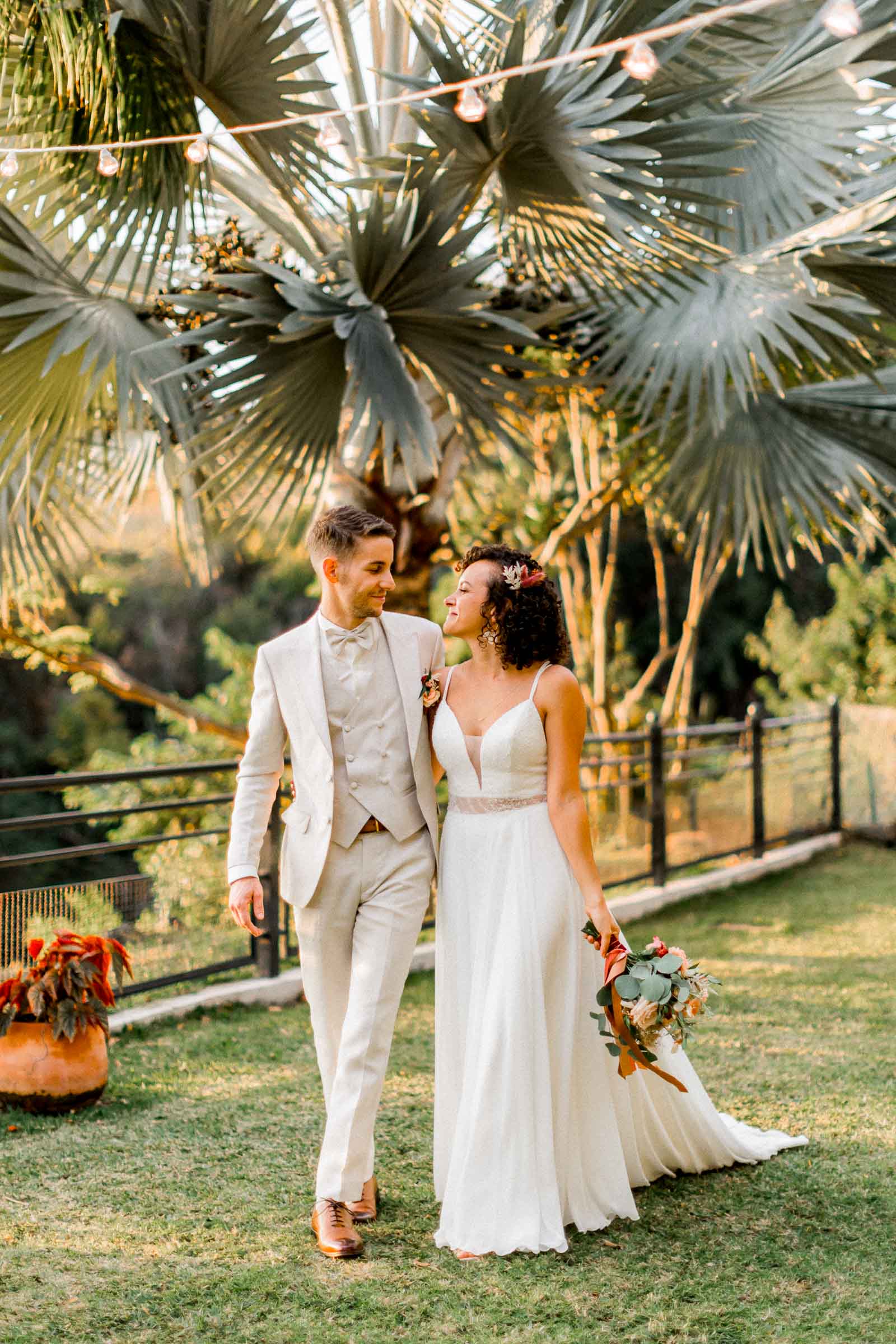 Photographie de Mathieu Dété, photographe de mariage à Saint-Pierre sur l'île de la Réunion 974, présentant un couple de marié marchant sous les palmiers du Jardin d'Ama