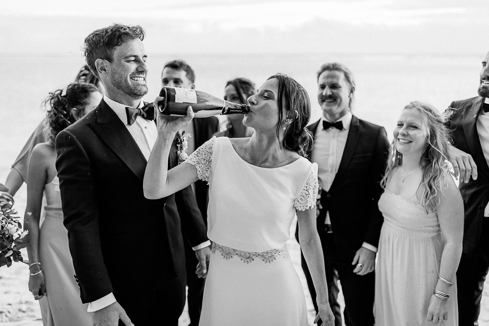 Photographie en noir et blanc de Mathieu Dété, photographe de mariage à Saint-Leu sur l'île de la Réunion 974, présentant une mariée buvant du champagne à la bouteille sur la plage