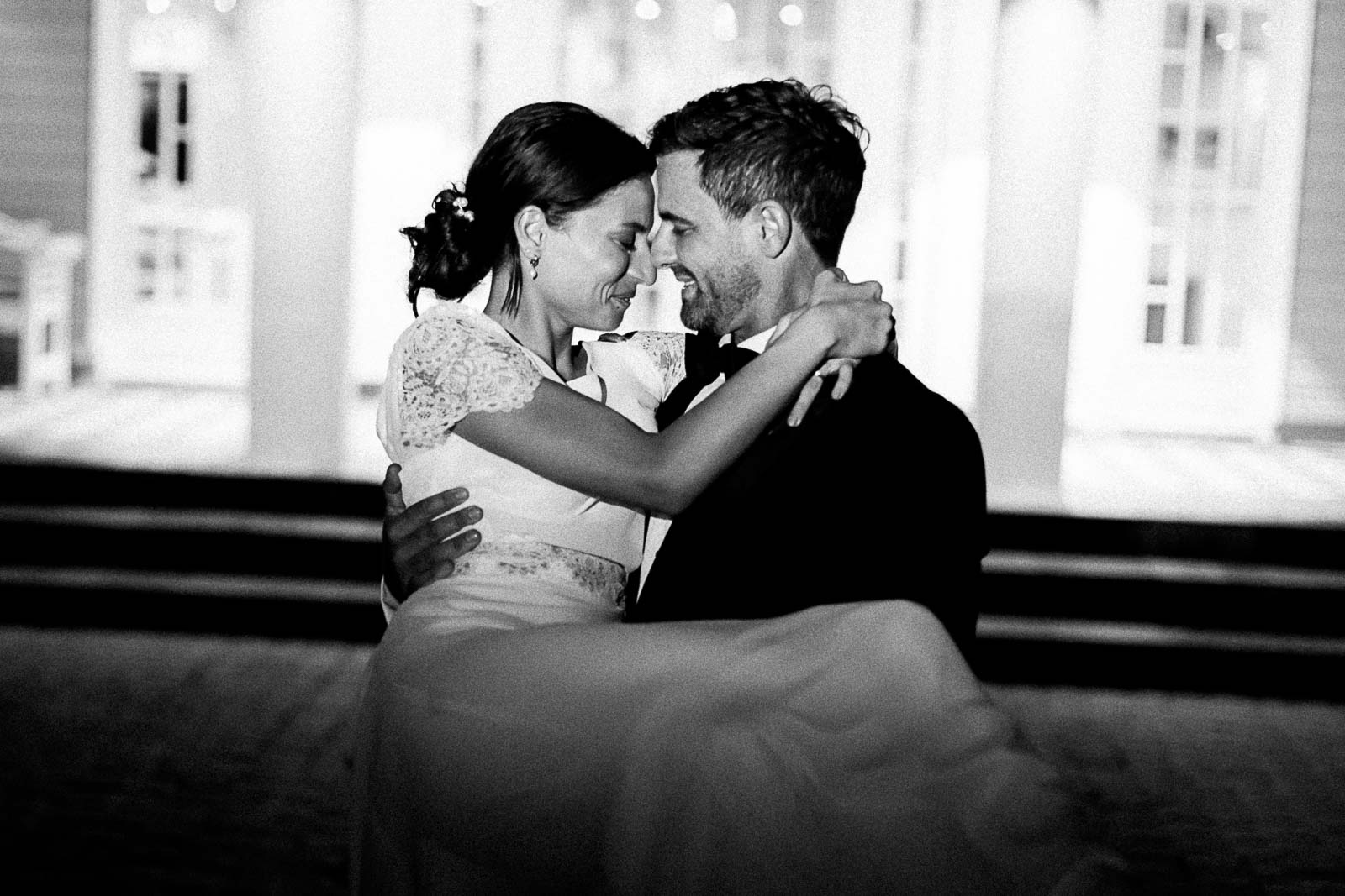 Photographie en noir et blanc de Mathieu Dété, photographe de mariage à Saint-Leu sur l'île de la Réunion 974, présentant un couple de mariés lors d'un mariage au LUX* Saint-Gilles, devant l'entrée, lorsque le marié porte sa femme dans les bras