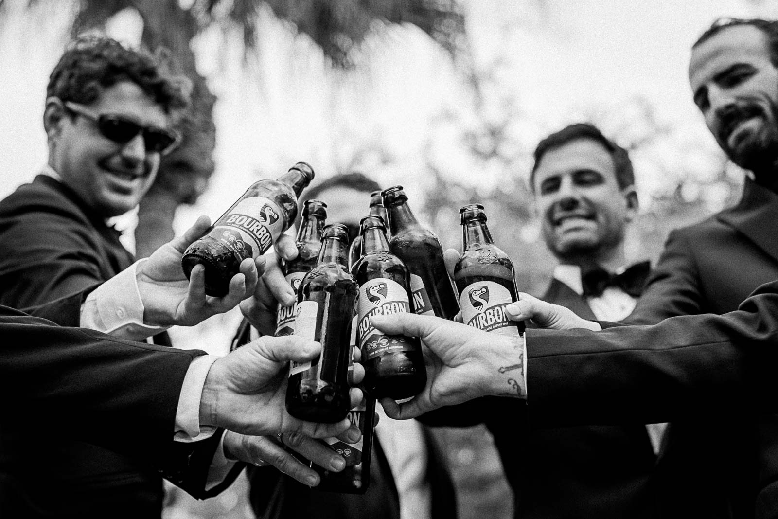 Photographie en noir et blanc de Mathieu Dété, photographe de mariage à Saint-Leu sur l'île de la Réunion 974, présentant le marié et ses amis qui trinquent à la Dodo, la bière locale réunionnaise, pendant les préparatifs du mariage