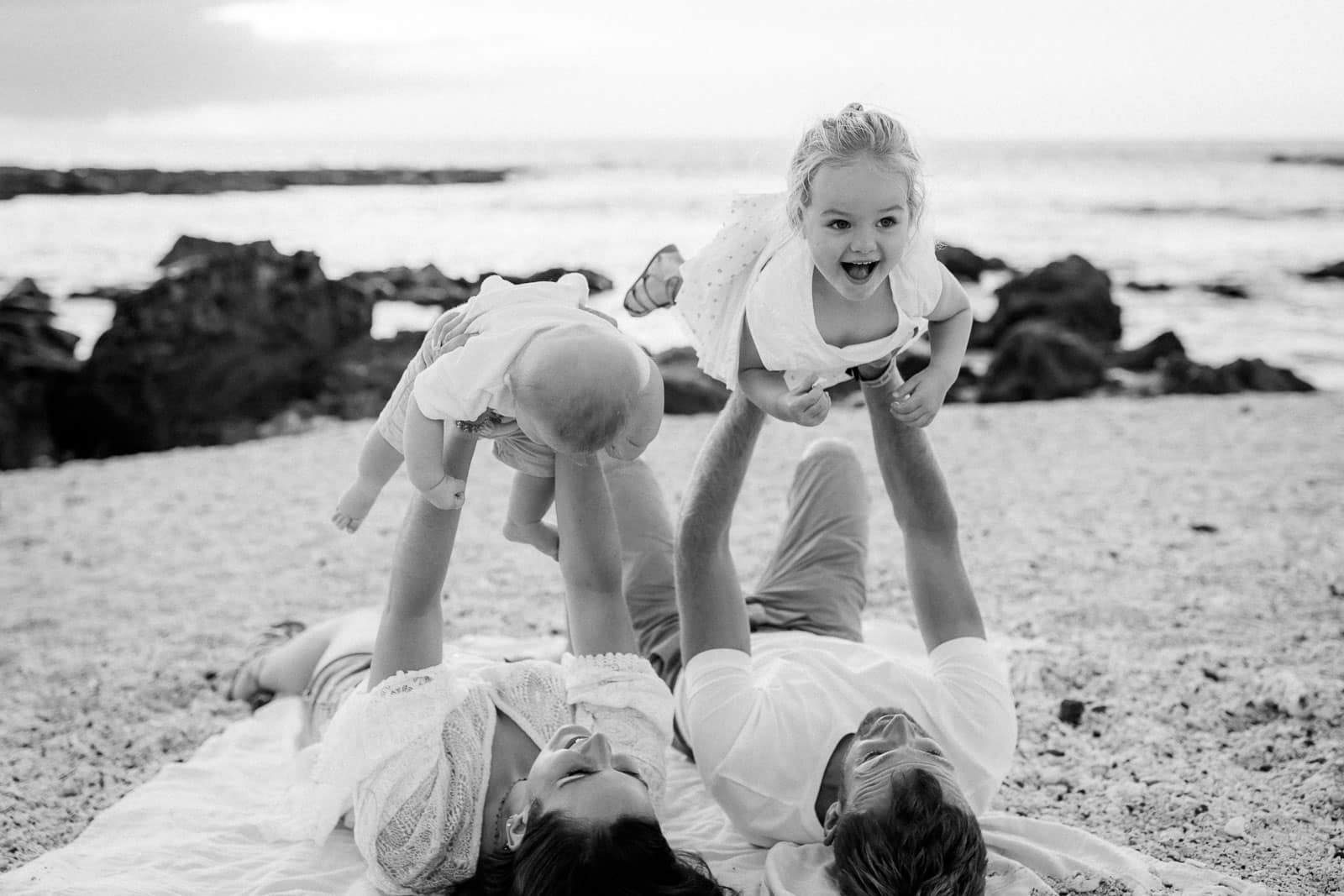 Photographie en noir et blanc de Mathieu Dété, photographe de mariage à Saint-Pierre de la Réunion 974, présentant une famille couchée sur le sable et qui rigole, à la Pointe au Sel