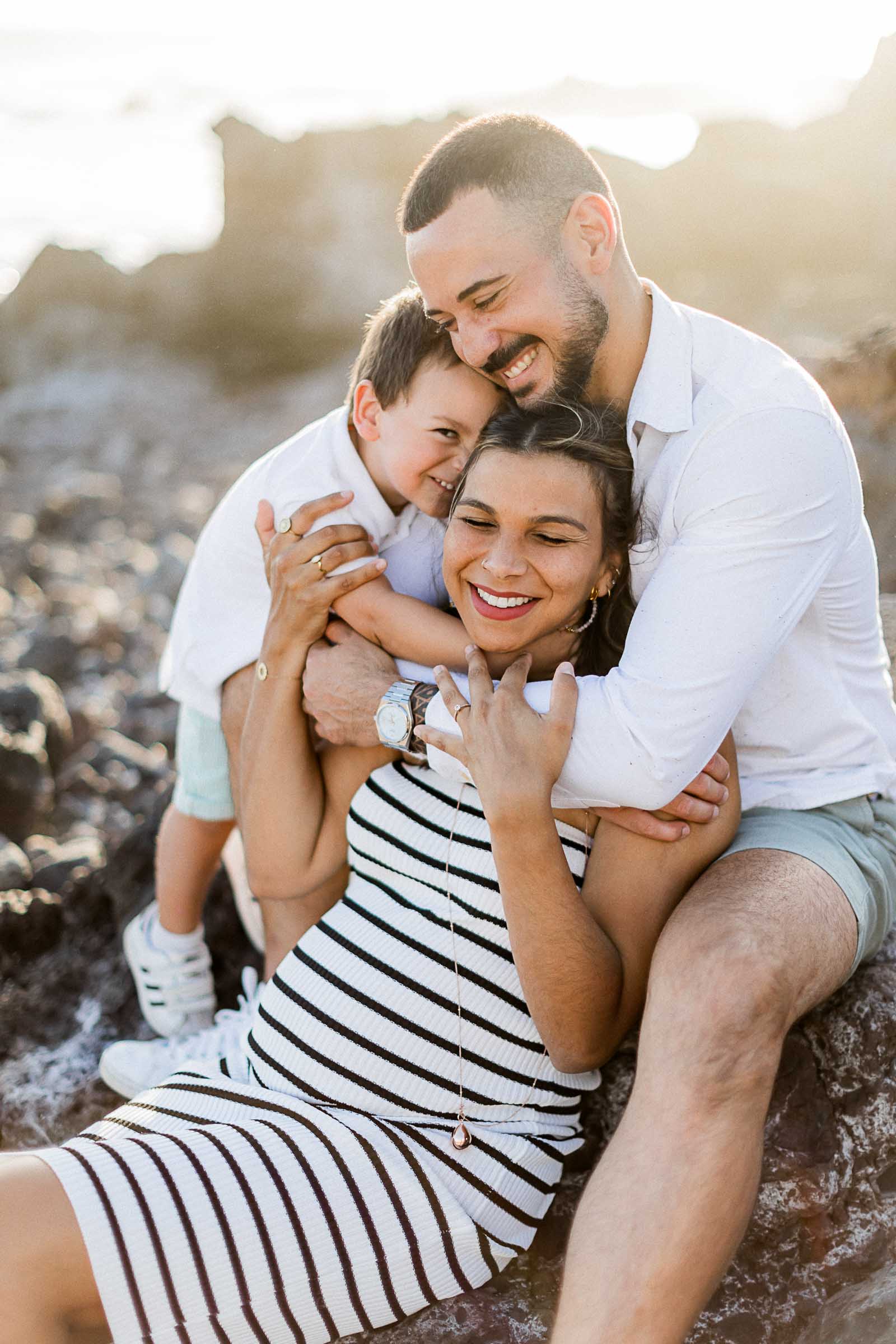 Photographie de Mathieu Dété, photographe de mariage à Saint-Pierre de la Réunion 974, présentant un câlin d'une famille avec son enfant en bord de mer au coucher du soleil, sur la Pointe des Trois Bassins